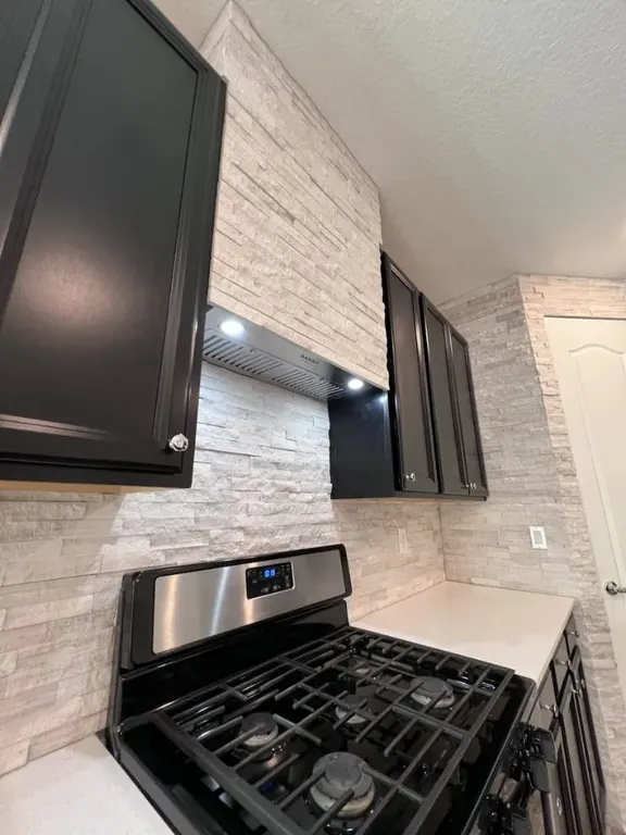Stone ledger kitchen backsplash with black cabinets and range hood in Jacksonville, FL